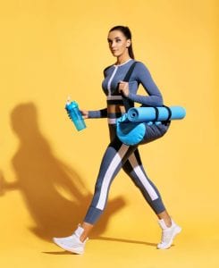 Best yoga mat bags - fit, pretty brunette woman on her way to yoga class carrying a mat and water bottle