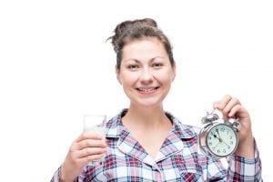 Woman in pajamas with a clock in her hand and drinking milk