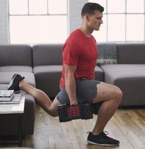Man doing squats with his leg on a sofa and holding adjustable dumbbells