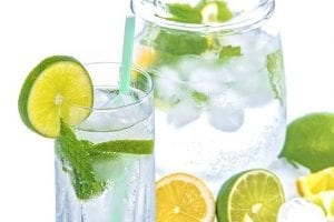 Jug of and glass water with straw, ice cubes, and lemon and lime slices