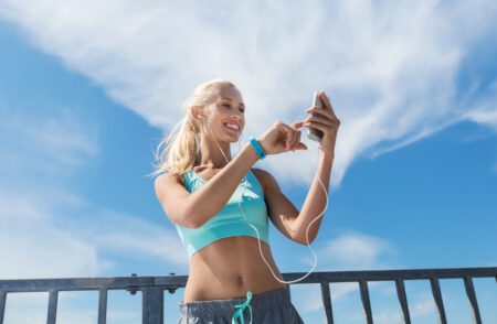happy, fit blonde woman exercising outdoors with smartphone and earphones