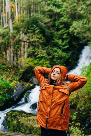 Girl in an orange jacket near a waterfall