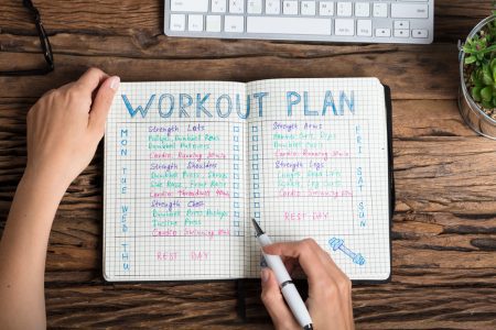 How to make fitness a habit - Close-up of a woman's hand writing a workout plan on a grid notebook