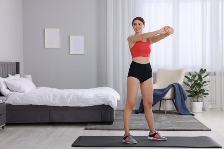 How to make fitness a habit - morning routine. Happy woman doing stretching exercise in her bedroom