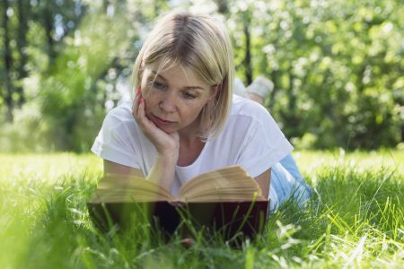 Young woman lying on grass in the park, reading a book.